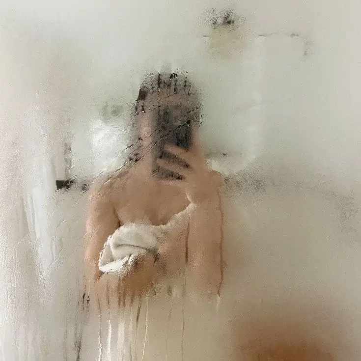 Девушка делает селфи через запотевшее зеркало в ванной комнате