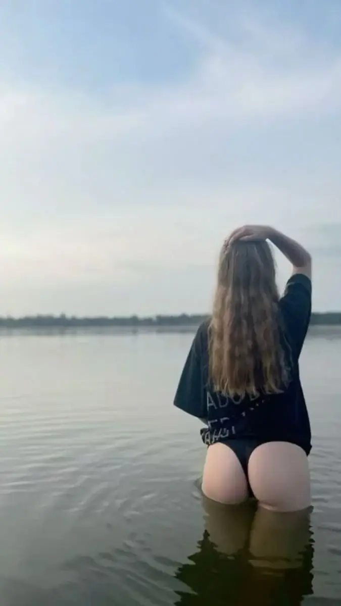 Девушка с волнистыми волосами стоит в воде на речке