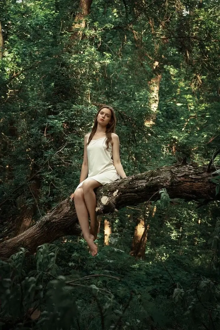 Девушка в коротком платье сидит на дереве как лесная нимфа