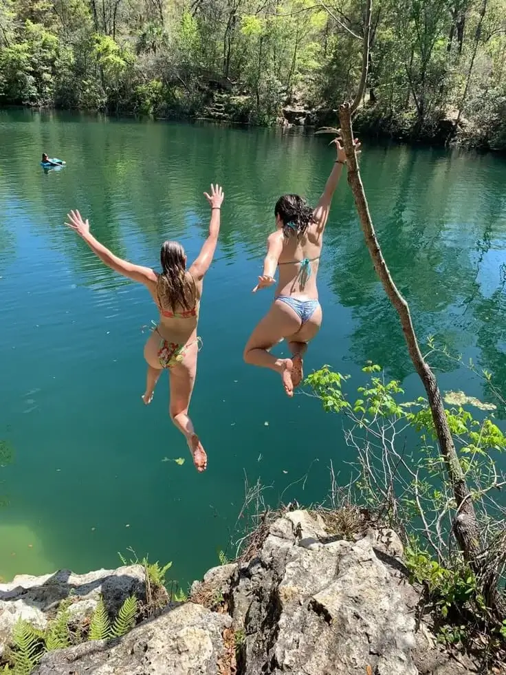 Две подруги в купальниках прыгают вниз с обрыва  в воду