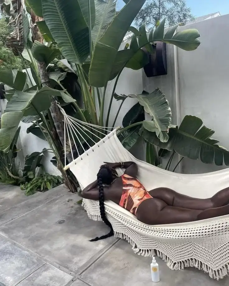 Негритянка с длинной косой в гамаке под листьями папоротника