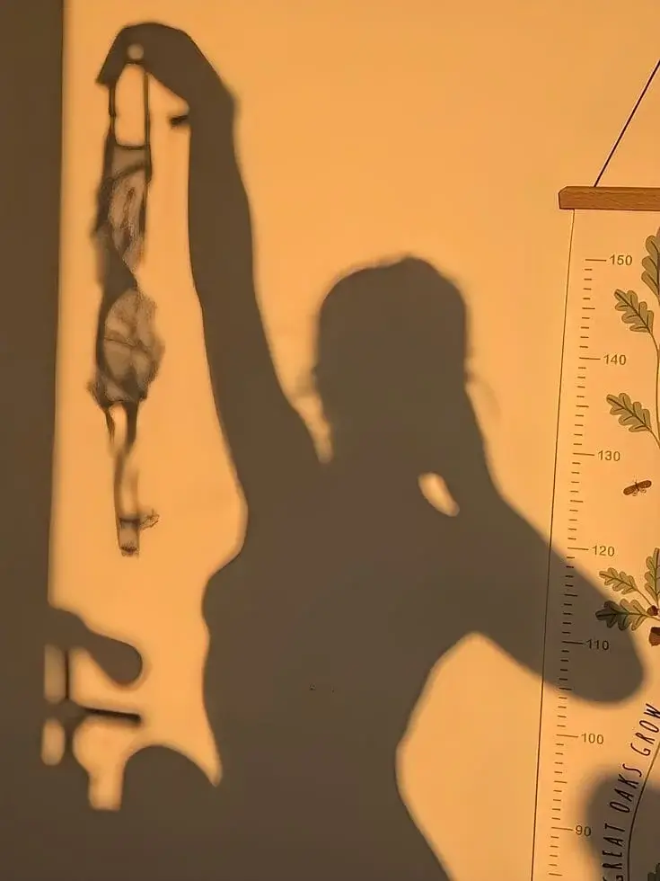 Тень от девушки на стене держит лифчик в руке